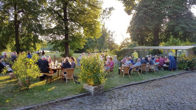 Gäste an Tischen im Garten, dahinter die Bäume des Eiswerder-Parks